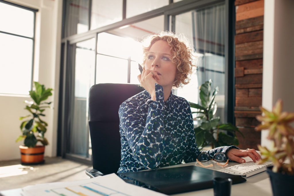 Portrait of young female designer sitting at her desk looking away and thinking.